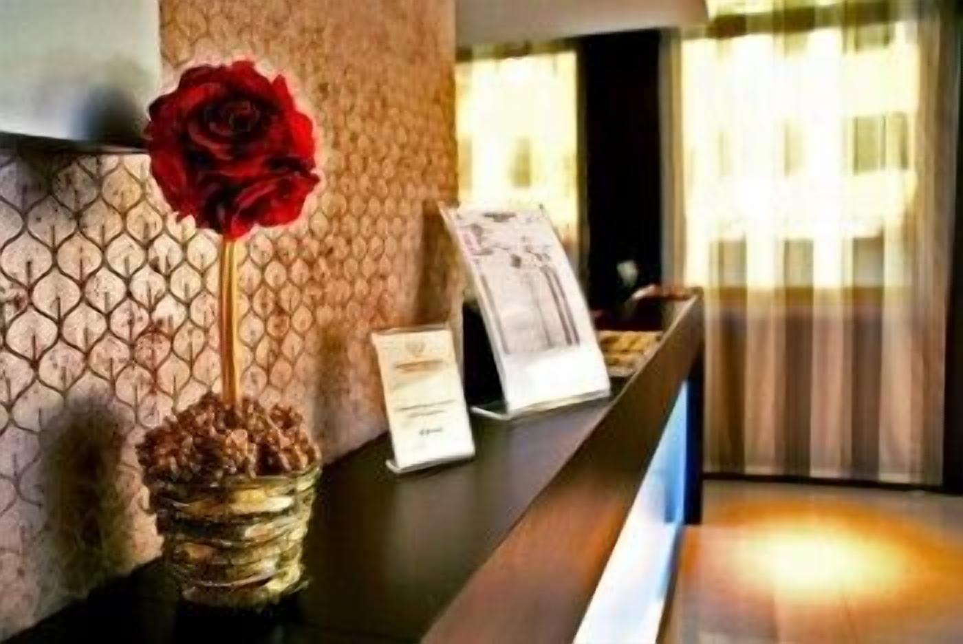 Un mostrador de recepción con un jarrón de rosas rojas, una placa con nombre y un menú.