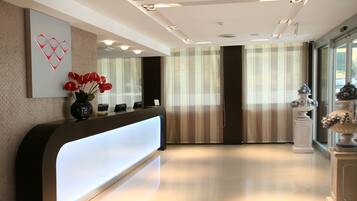 A modern reception area with a curved reception desk, a vase of red flowers, a decorative wall piece, and a large window with striped curtains.