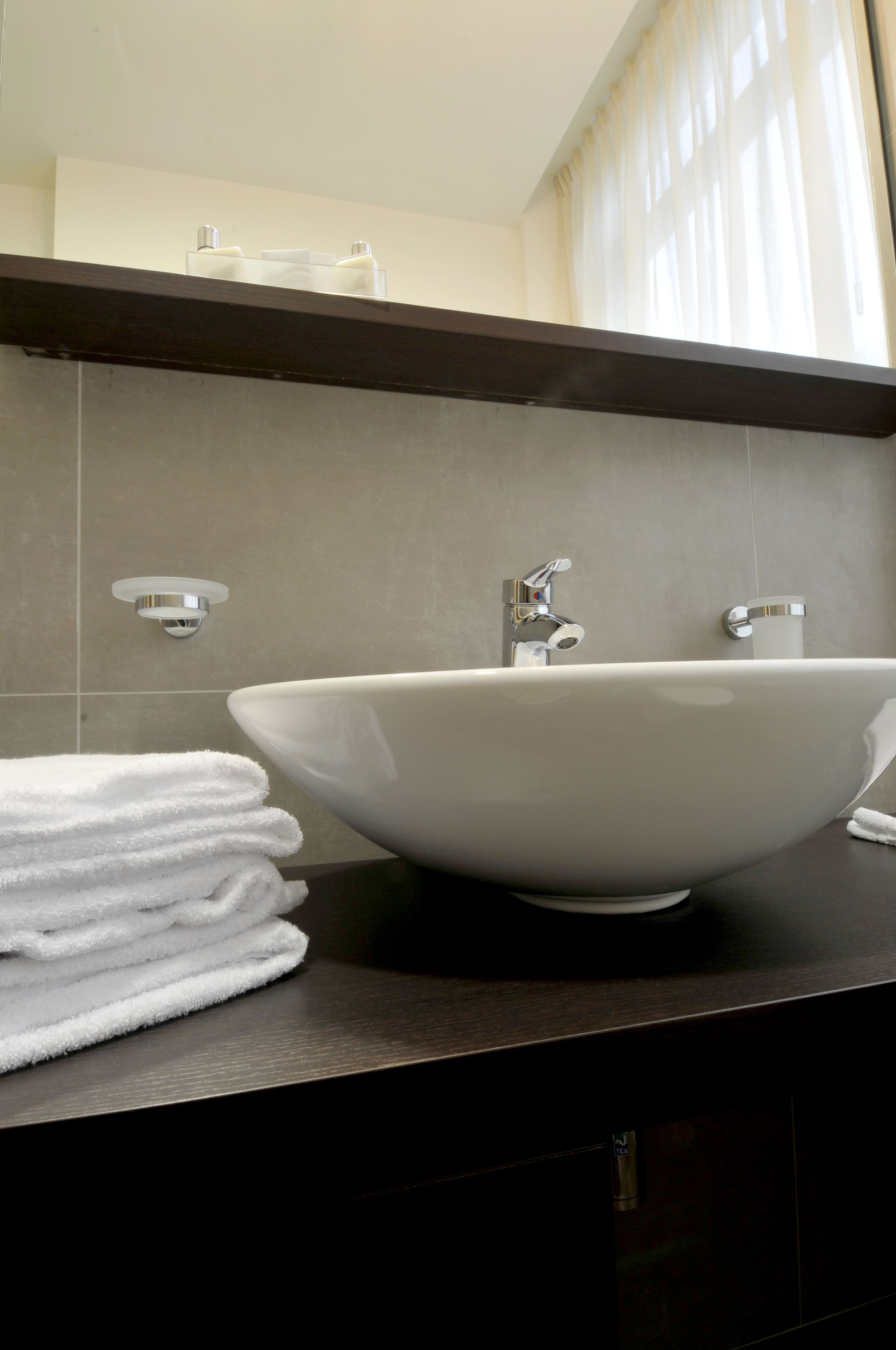 Ein Badezimmer mit einem großen, weißen Waschtischbecken, einer dunklen Arbeitsplatte und einem Stapel weißer Handtücher.