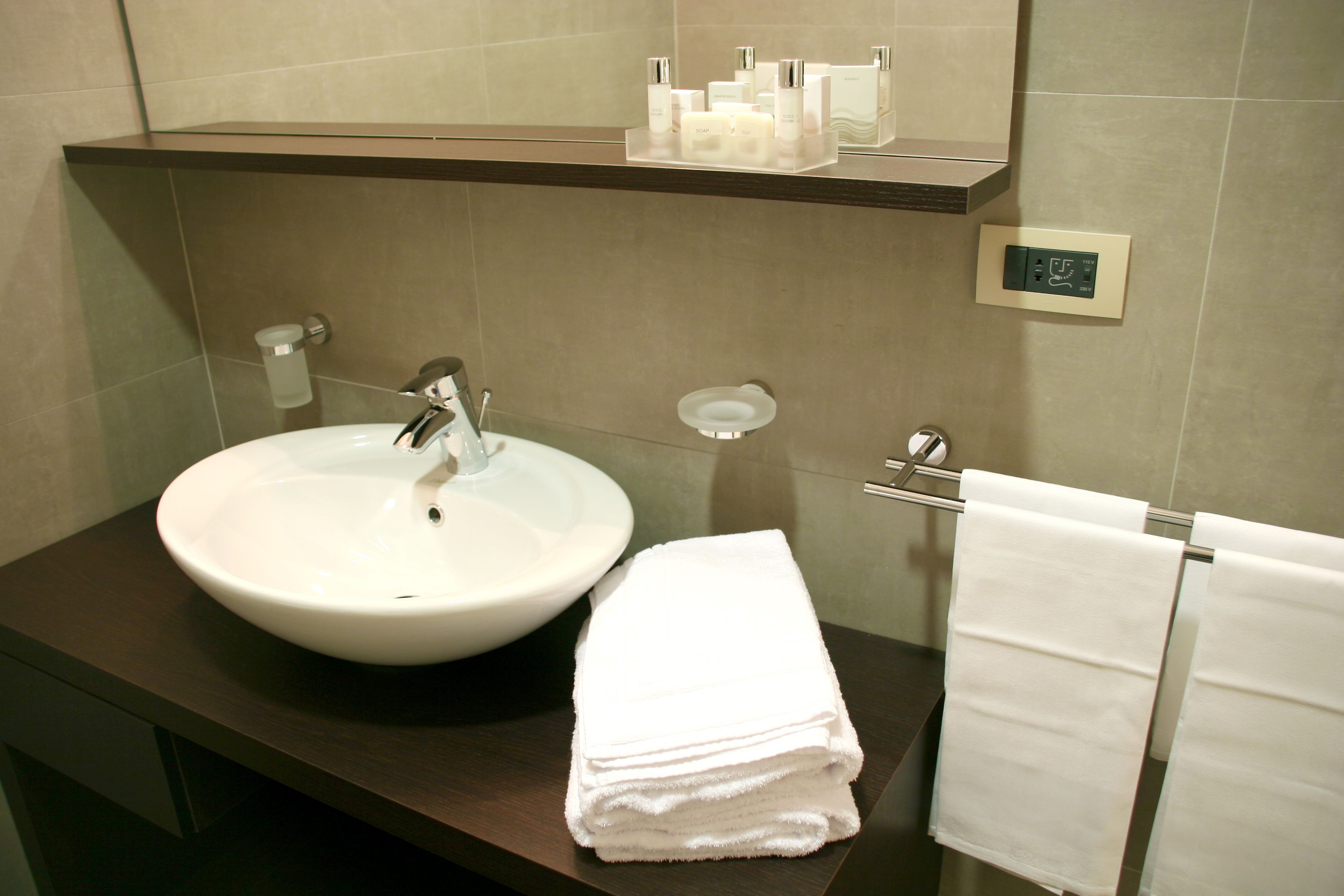 A bathroom with a white sink, a towel rack with folded towels, and a shelf with toiletries.