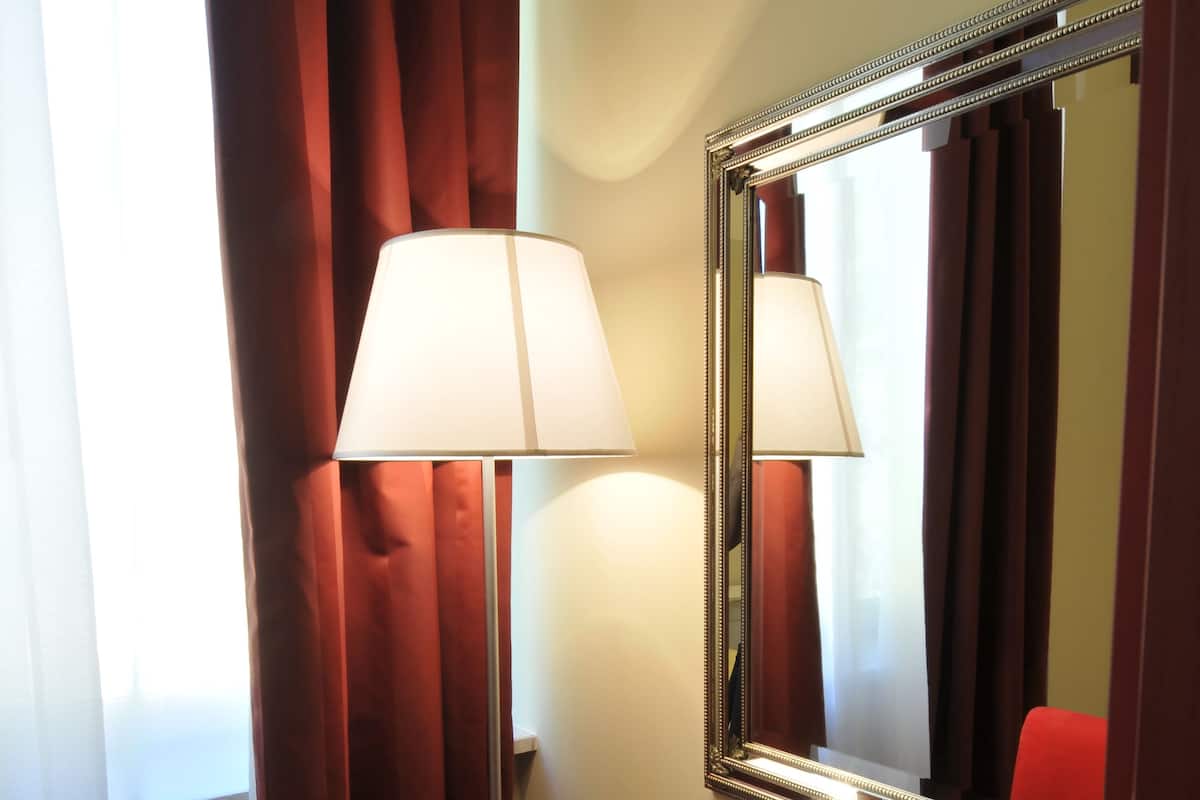 A hotel room with a wooden desk, a red chair, a lamp, and a mirror.