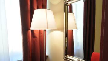 A hotel room with a wooden desk, a red chair, a lamp, and a mirror.
