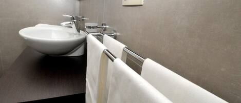 A modern bathroom with a large sink, towel rack, and a wall-mounted thermostat.