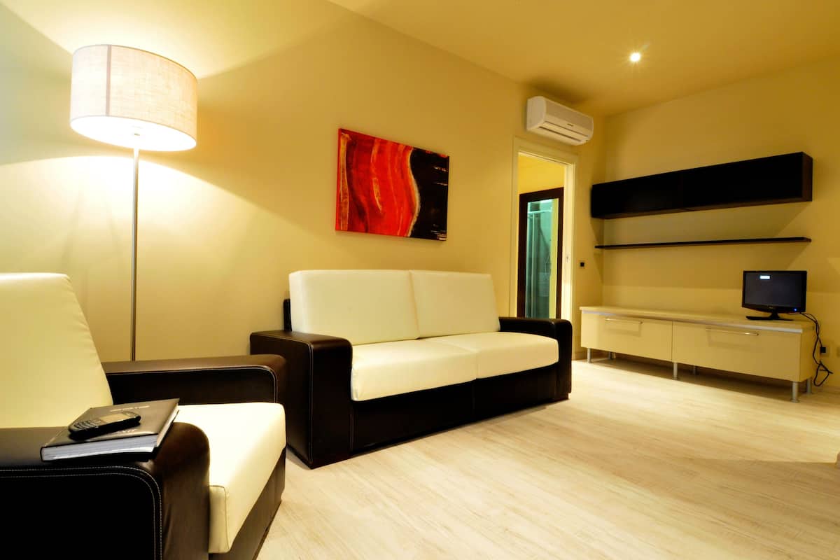 A modern living room with a sofa, a side table, a lamp, a flat-screen TV, and a painting on the wall.