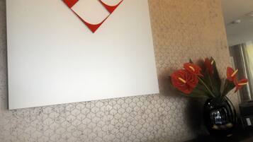 Un mur orné d’une œuvre d’art géométrique et un vase contenant des fleurs rouges.