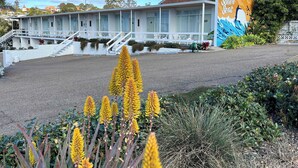 Un motel orné d’une grande fresque murale faisant la publicité des îles de la mer du Sud. On y trouve un escalier menant à l’entrée, un espace extérieur couvert avec des sièges, et une pelouse bien entretenue.