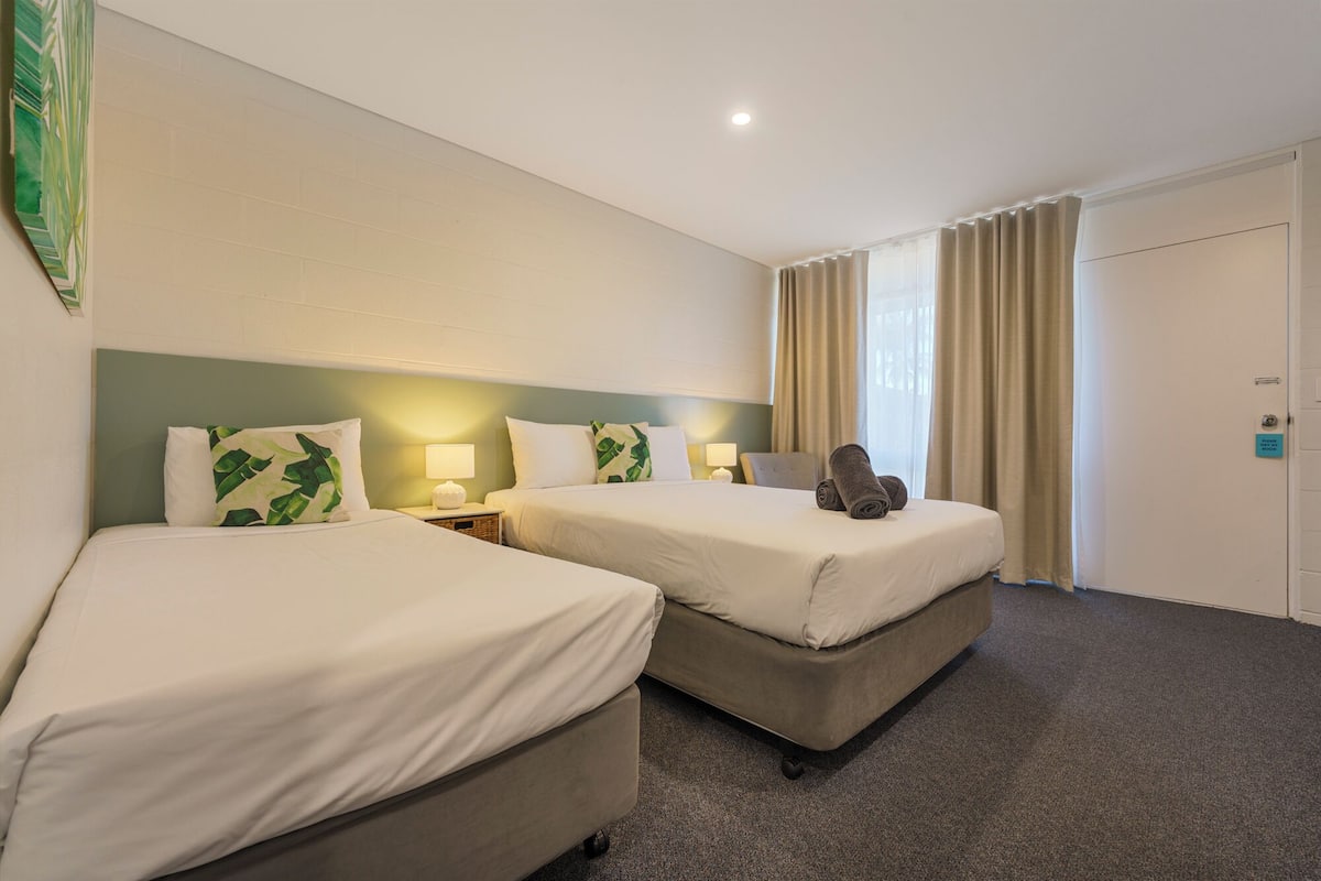 A hotel room with two beds, a nightstand with lamps, and a door with a sign.