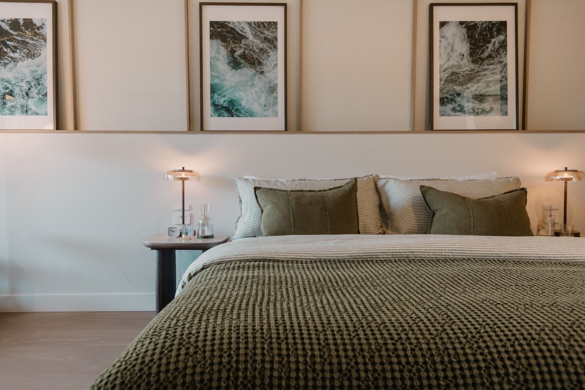 A hotel room with a bed, two bedside tables, and three framed artworks on the wall.
