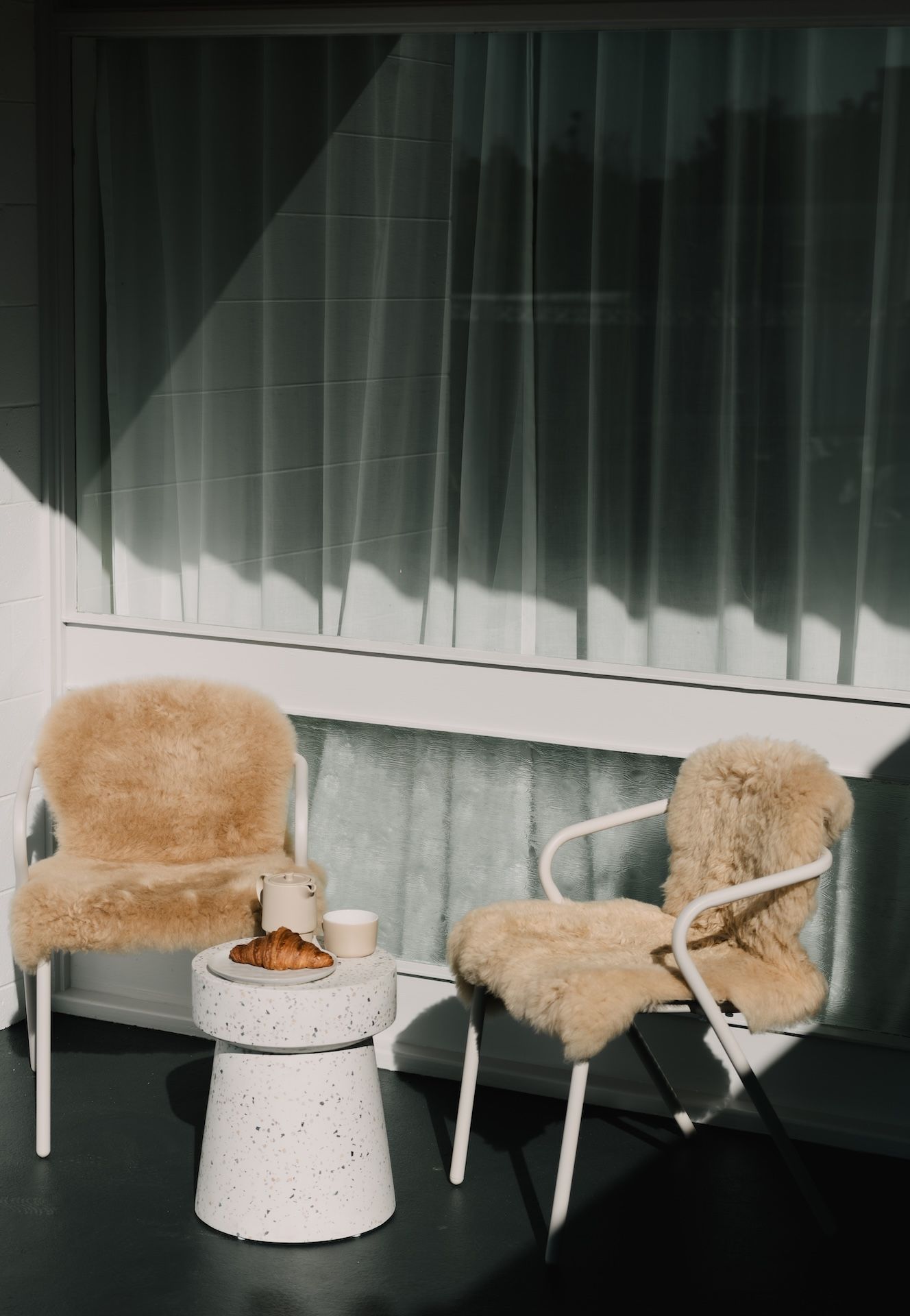 Two chairs with fluffy cushions, a small table with a croissant, and a window with curtains.