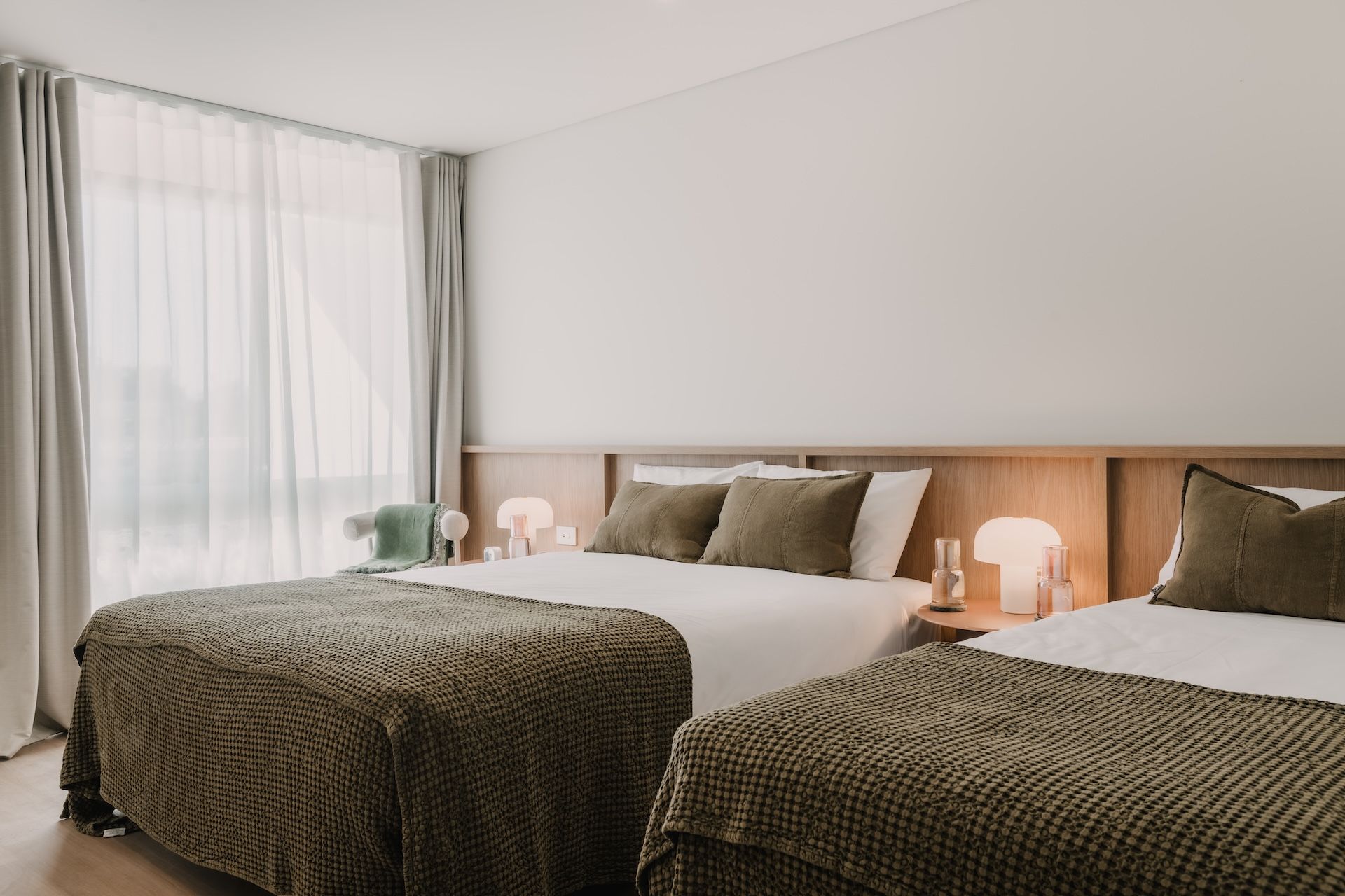 Une chambre d’hôtel avec deux lits, une table de chevet, une lampe et une fenêtre avec des rideaux.