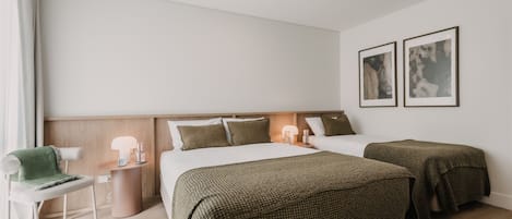 A hotel room with two beds, a chair, bedside tables, and artwork on the wall.