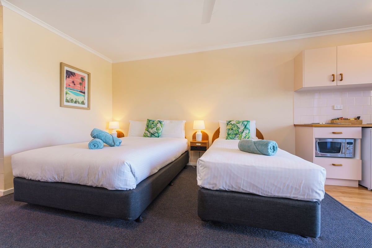 A hotel room with two beds, a kitchenette, and a painting on the wall.