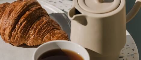 Un croissant, una tetera y una taza de té sobre un plato de cerámica con motas.
