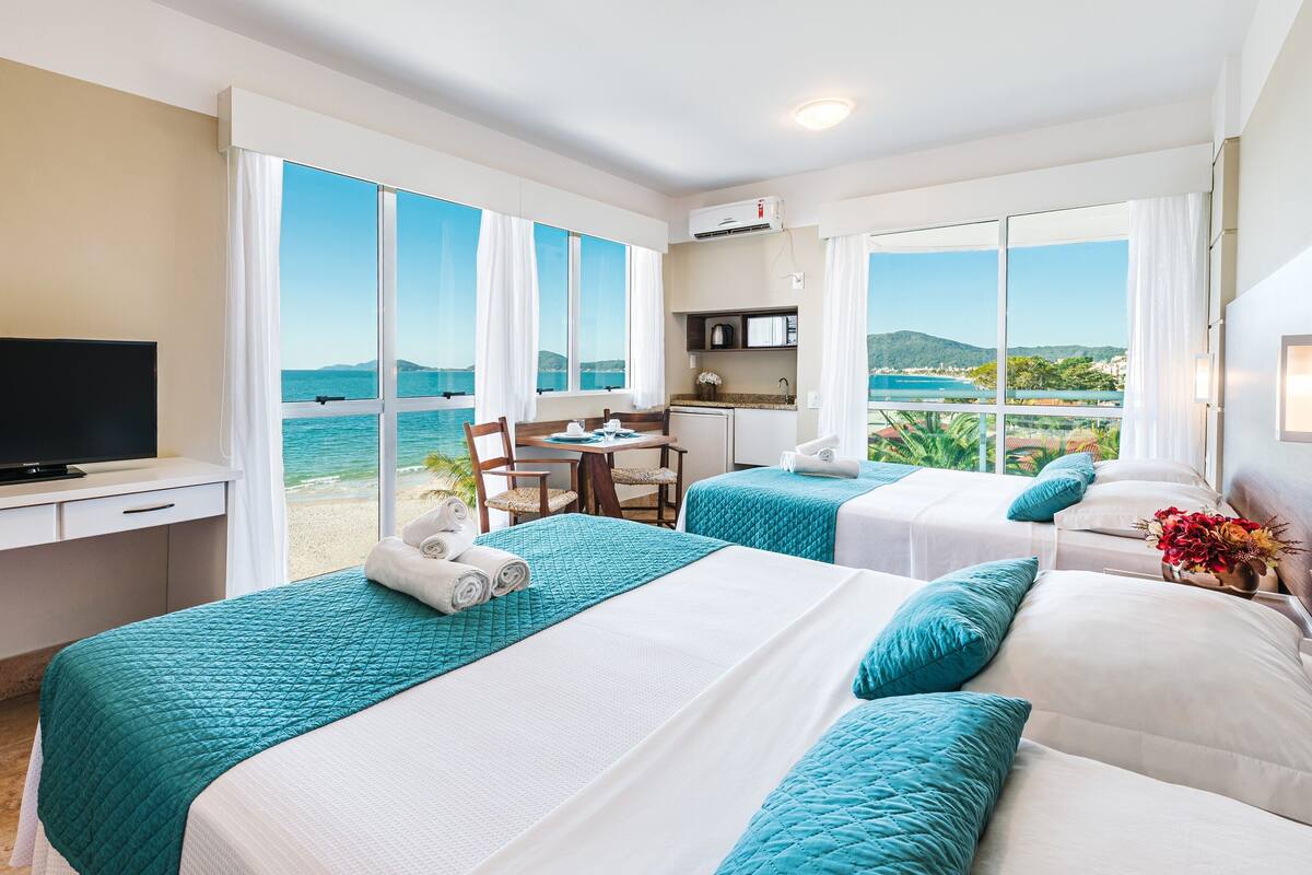 Une chambre d’hôtel avec deux lits, un bureau, une télévision et une vue sur la mer.