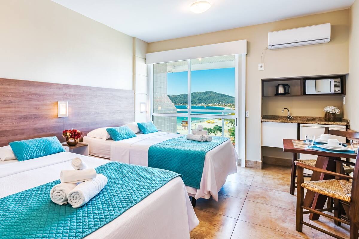 Une chambre d’hôtel avec deux lits, une vue sur la mer, une kitchenette et un coin repas.