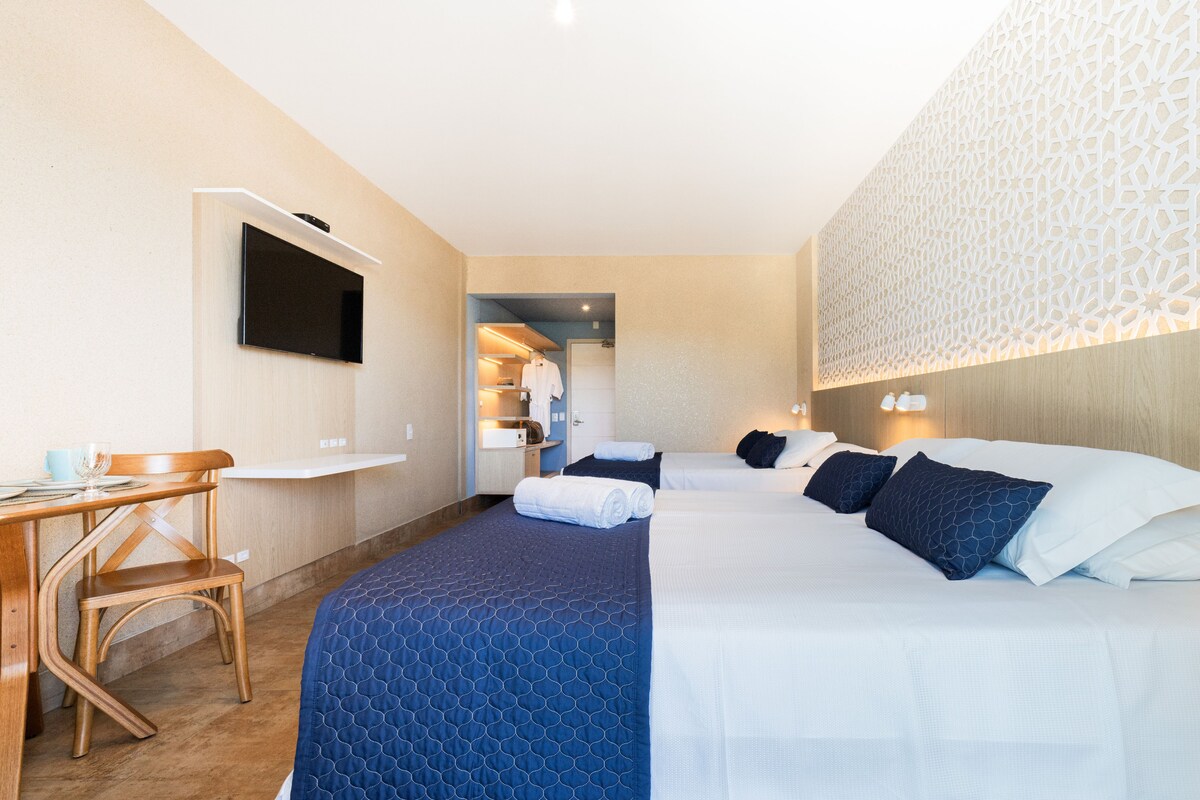 A hotel room with a bed, a desk, a TV, and a bathroom visible through an open door.