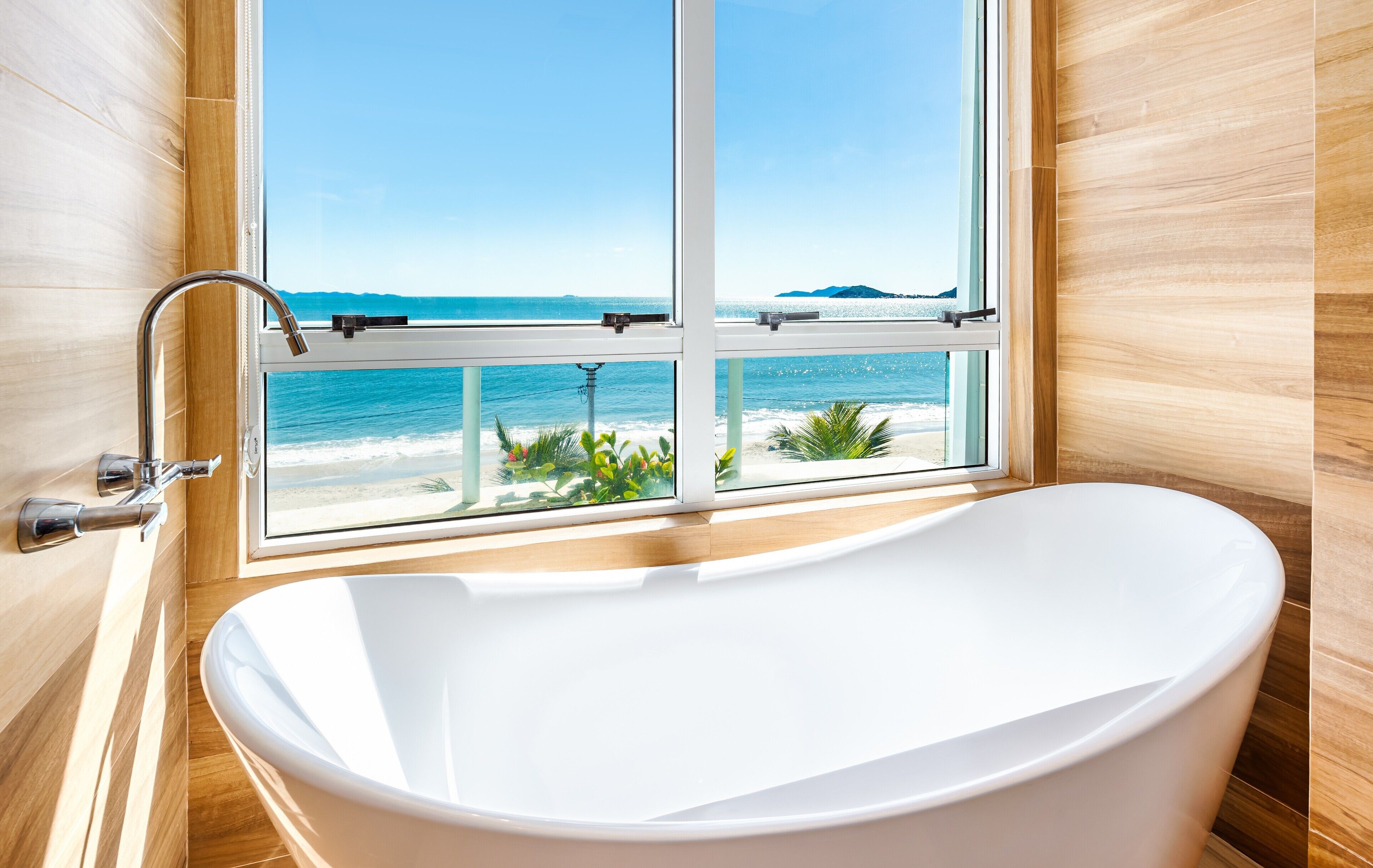 Un bagno moderno con una grande vasca, una finestra vista spiaggia e pareti in legno.