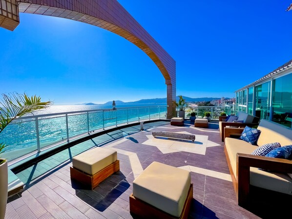 A rooftop terrace with a clear view of the sea, furnished with sofas and potted plants.
