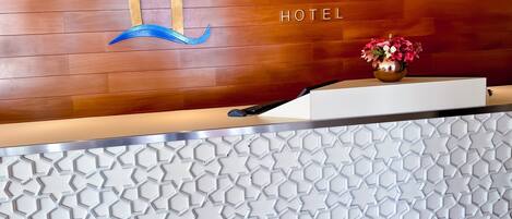 Ein Hotelrezeptionstresen mit Wandverkleidung aus Holz, dem großen 'P'-Logo und einer Vase mit Blumen.