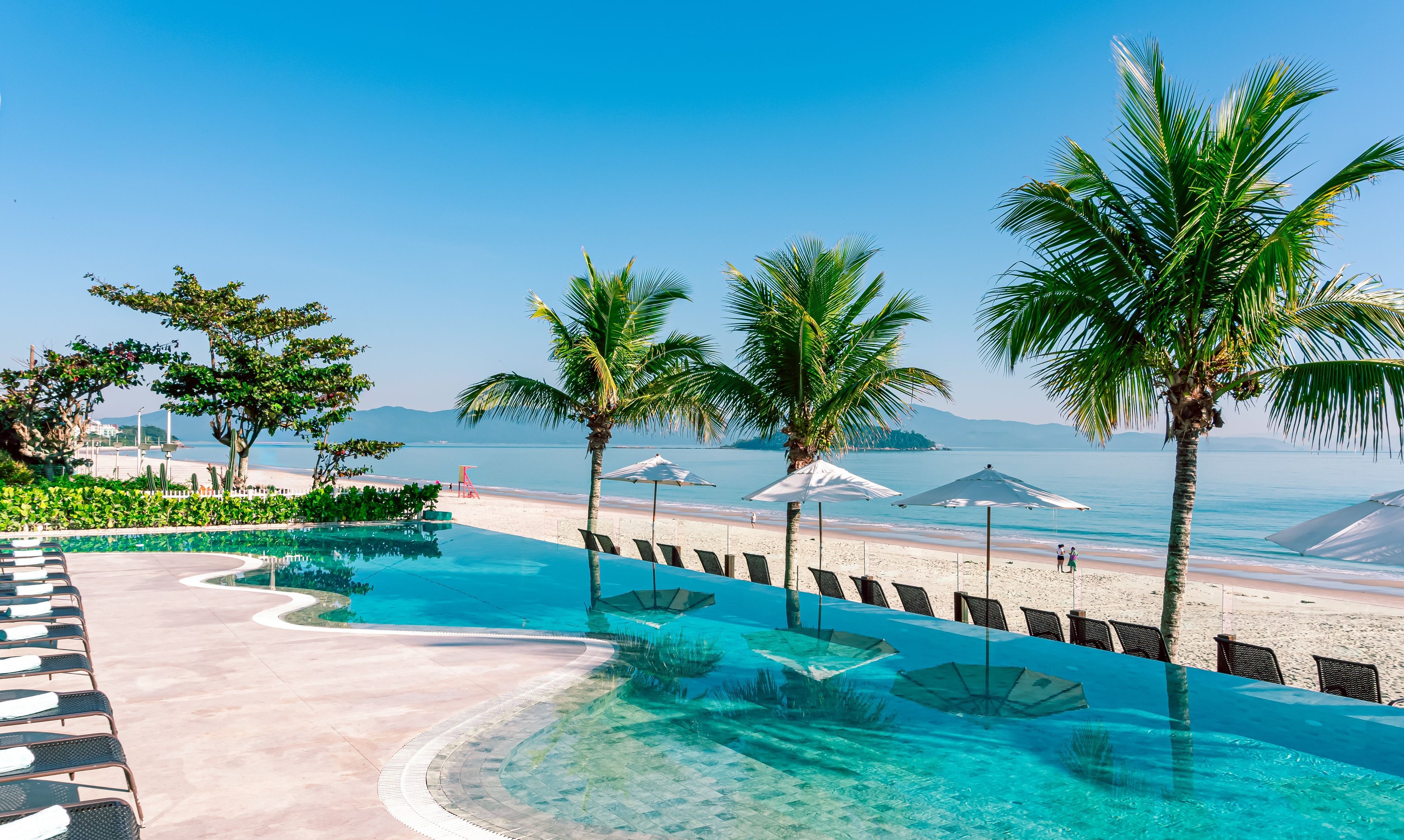 A poolside area with clear water, lounge chairs, and umbrellas.