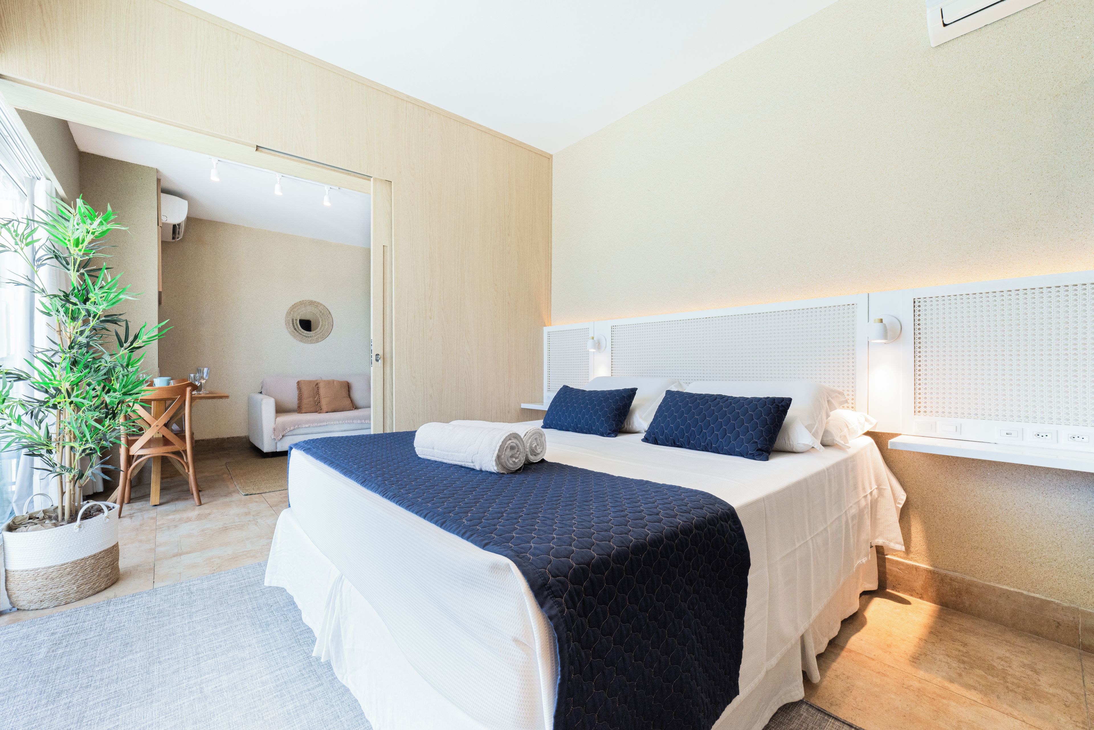 Camera d'albergo moderna con un letto grande, una pianta in vaso e un angolo salotto con tavolo e sedie.
