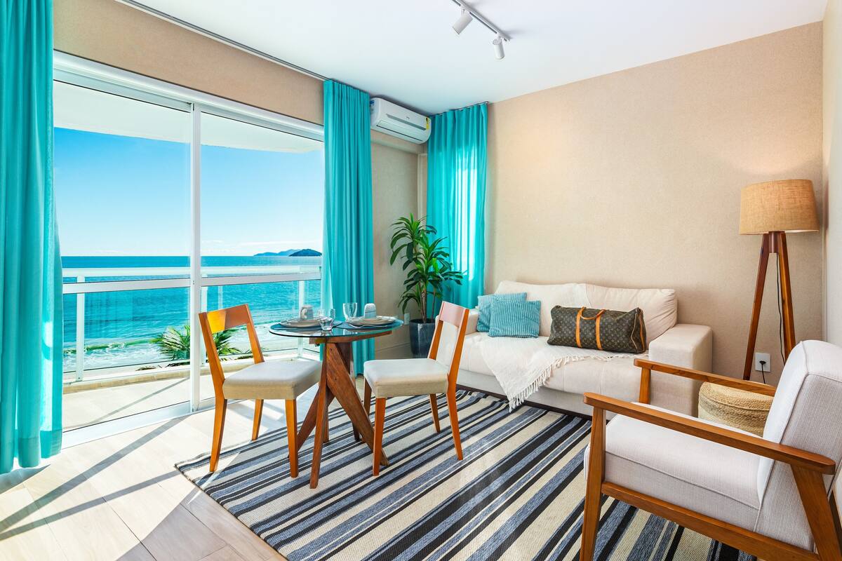 Un balcon avec vue sur l’océan, un coin repas avec des chaises et une table, un canapé avec des coussins et une lampe sur pied.