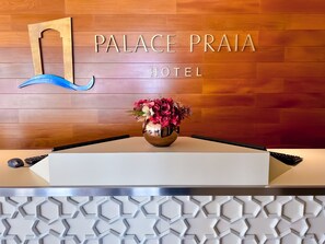 A hotel reception desk with a wooden wall behind it displaying the name "PALACE PRAIA HOTEL". - Palace Praia Hotel (Florianópolis)