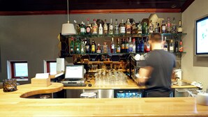 A bar area with a bartender preparing drinks, a computer monitor, and a variety of liquor bottles on shelves. - Fosshotel Hekla (Selfoss)