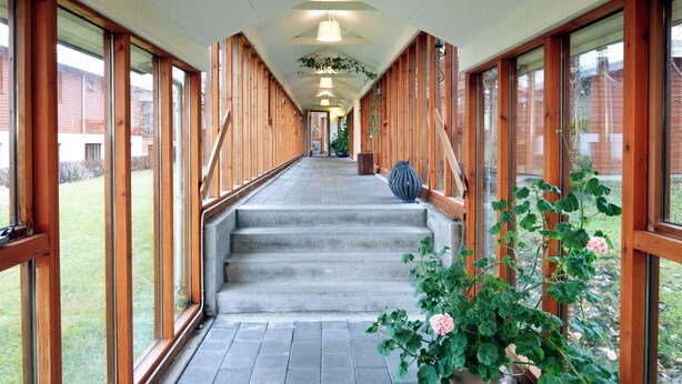 A covered outdoor corridor with wooden walls and large windows, leading to a staircase. - Fosshotel Hekla (Selfoss)