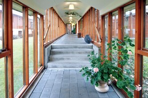 A covered outdoor corridor with wooden walls and large windows, leading to a staircase. - Fosshotel Hekla (Selfoss)