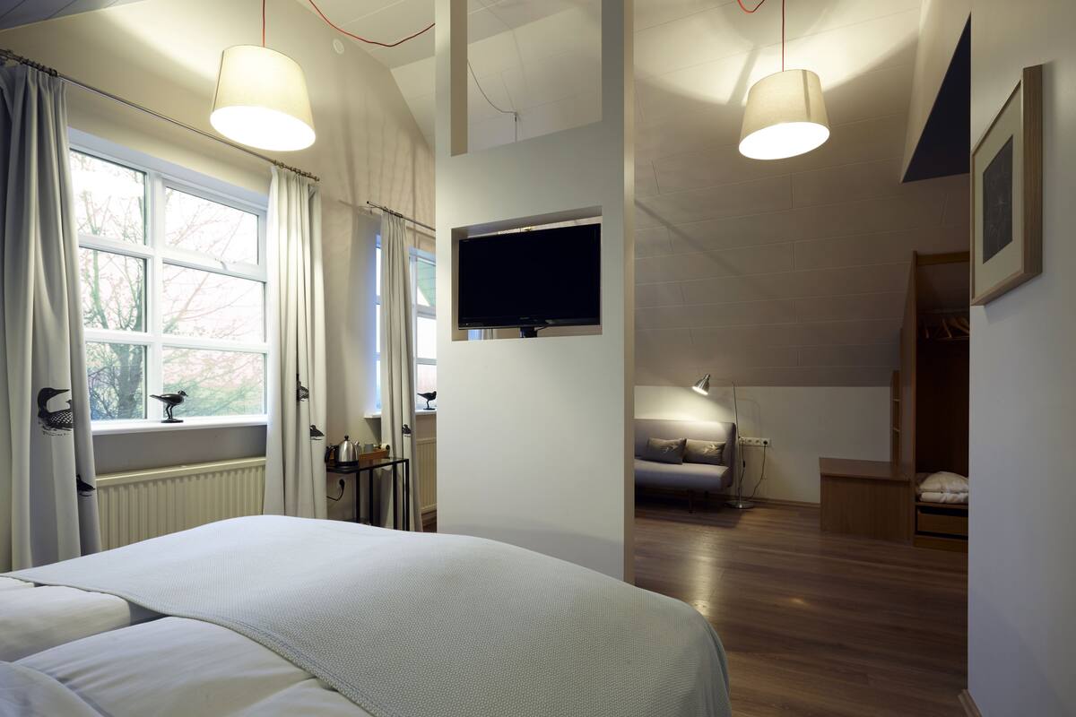 Un dormitorio con una cama grande, un televisor montado en la pared y un ventanal con cortinas.