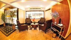 A lobby with a checkered floor, two leather armchairs, a coffee table, a vase with flowers, and a potted plant.