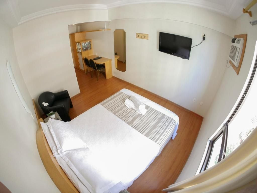 Habitación de hotel pequeña con cama, escritorio, silla, televisor y ventana.