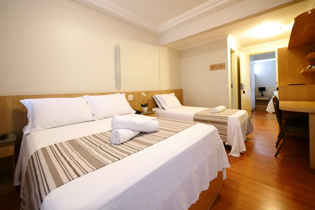 Une chambre d’hôtel avec deux lits, une tête de lit en bois, une petite table avec une lampe et une chaise.