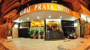 The exterior of the Icarai Praia Hotel with a curved entrance, potted plants, and a car parked in front.