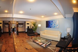 Un hall d’entrée moderne avec un sol en marbre, une table basse en verre sur laquelle sont posés des magazines, un canapé blanc et un tableau abstrait bleu accroché au mur.
