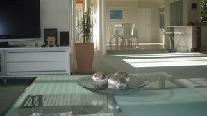 A modern living room with a flat-screen TV, a dining area with a glass table, and a kitchen with bar stools. - Seascape Villa Bed & Breakfast (Tauranga)