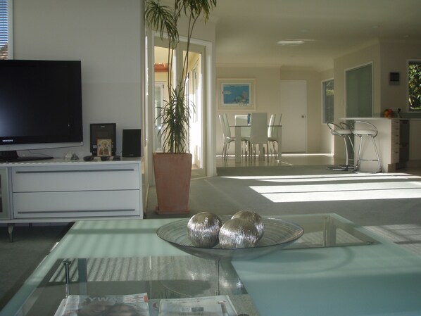 A modern living room with a flat-screen TV, a dining area with a glass table, and a kitchen with bar stools. - Seascape Villa Bed & Breakfast (Tauranga)