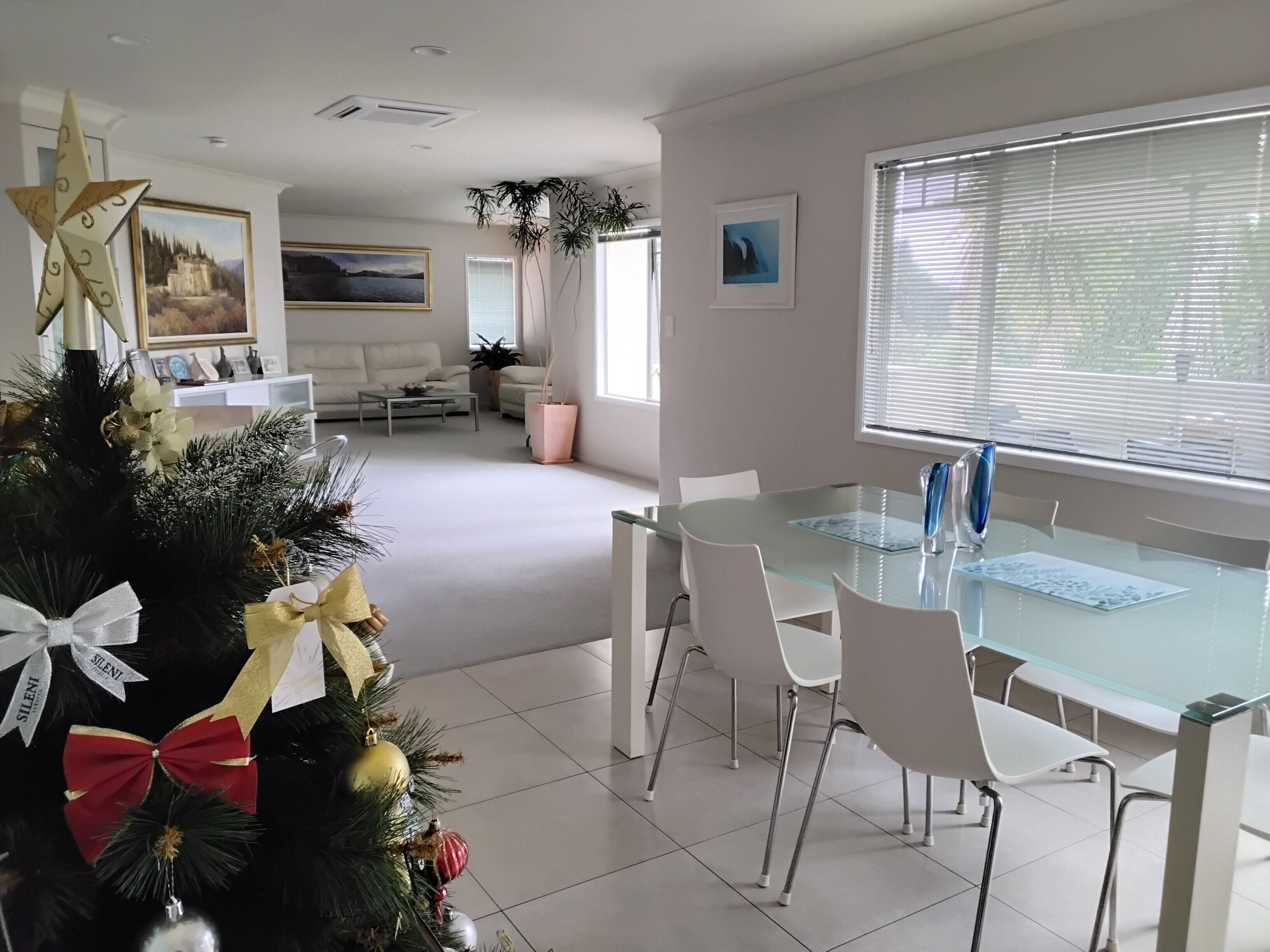 Un comedor moderno con una mesa de vidrio y sillas blancas, un árbol de Navidad adornado y un cuadro en la pared.