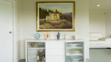 Un mueble blanco con puertas de vidrio y un cuadro de una casa en la pared.
