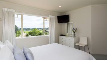 A bedroom with a large bed, a dresser, a chair, a TV, and a window with curtains.