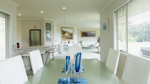 A modern dining area with a glass table, white chairs, and two blue glass vases. - Seascape Villa Bed & Breakfast (Tauranga)