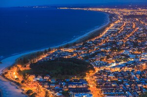 An aerial view of a coastal town at night with a beach, roads, and residential buildings.