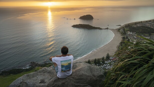 A person sitting on a rock overlooking a beach with a sunset in the background. - Seascape Villa Bed & Breakfast (Tauranga)