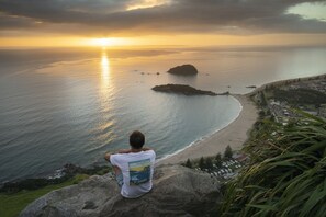 A person sitting on a rock overlooking a beach with a sunset in the background. - Seascape Villa Bed & Breakfast (Tauranga)