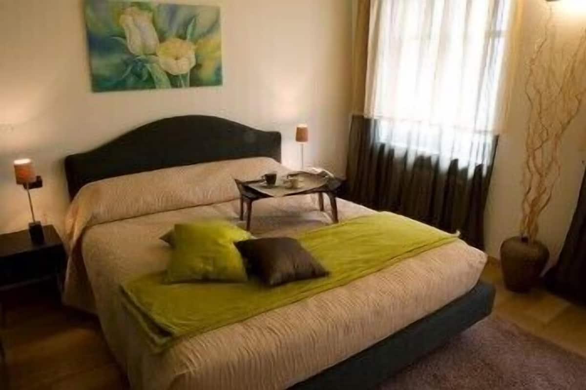 A neatly arranged bedroom with a bed, a bedside table, a lamp, and a painting on the wall.