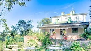 A two-story house with a covered porch, surrounded by a well-maintained garden and outdoor seating area. - Drottning Victorias Hotell och Vilohem (Borgholm)