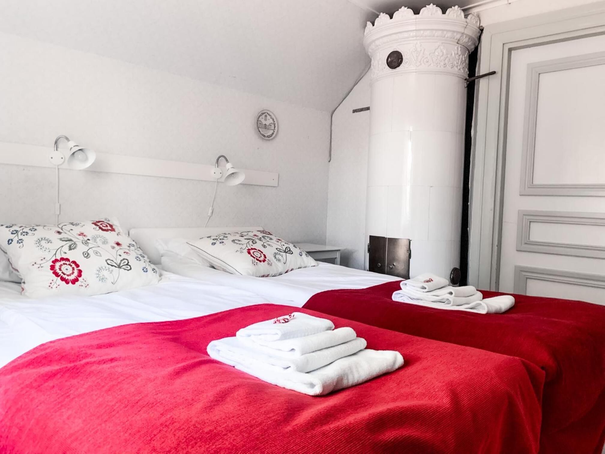 A hotel room with two beds, each with a red bedspread and white pillows, a white headboard, and a white wardrobe.