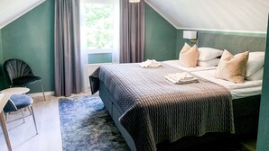A bedroom with a bed, a chair, a table, and a window with curtains. - Drottning Victorias Hotell och Vilohem (Borgholm)