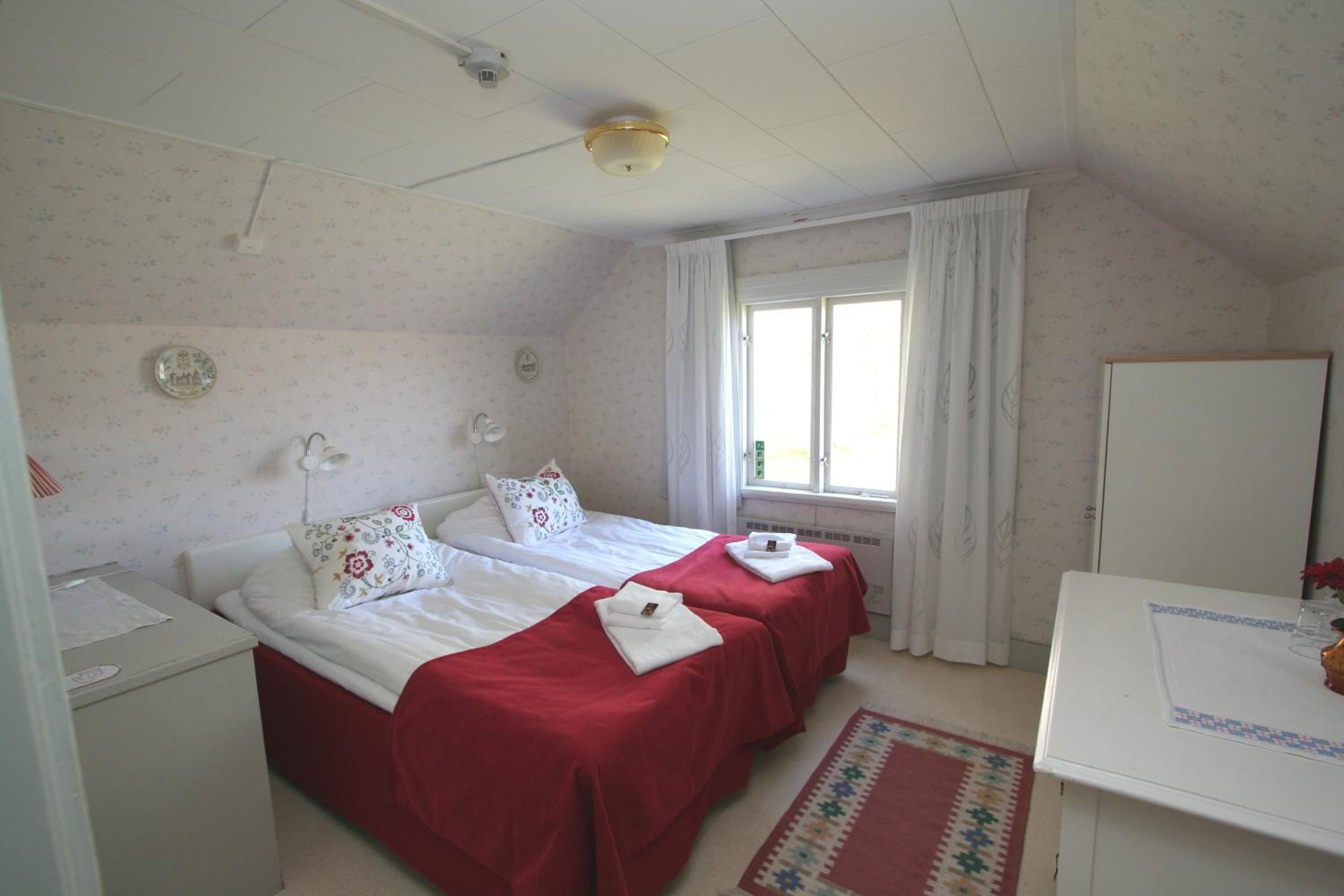 A bedroom with two beds, a desk, and a window with curtains.